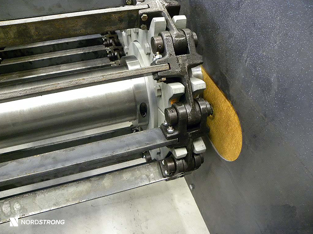 Close-up view of an industrial drag conveyor sprocket and chain system connected to a metal shaft inside a housing.